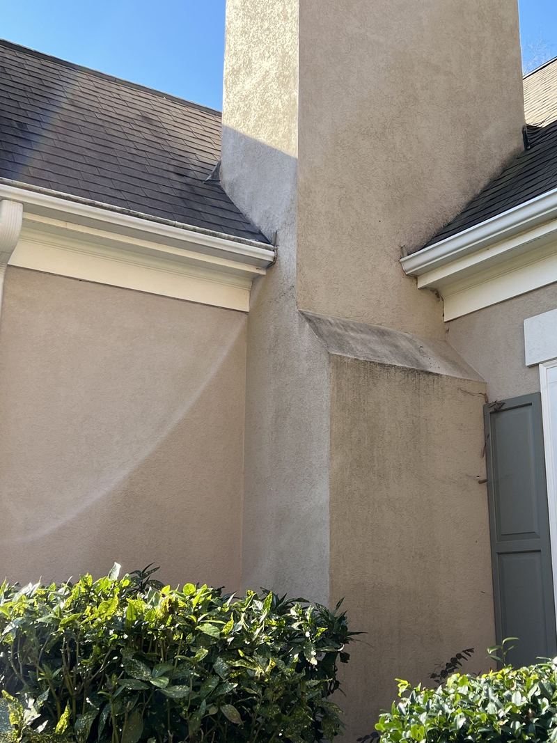 A stucco house wall streaked dark under the eaves