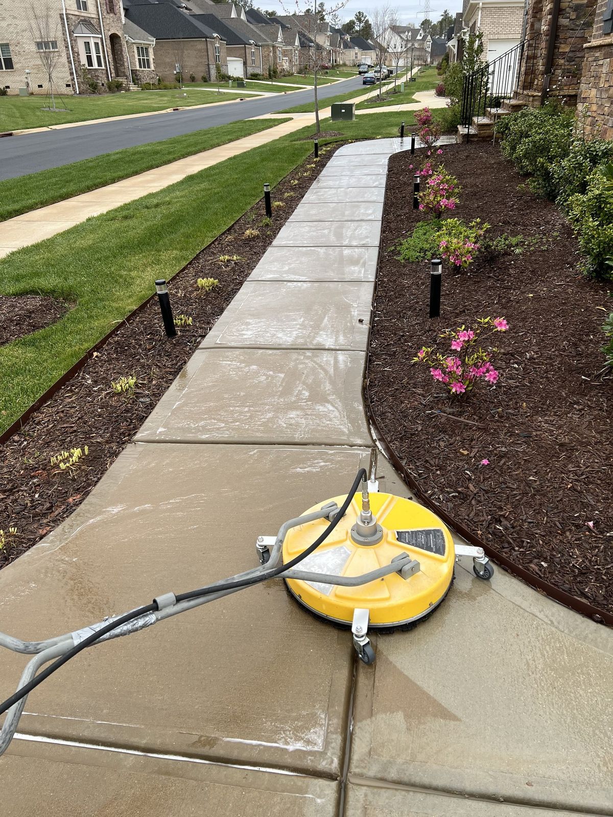 A surface cleaner part way along a walkway, cleaned concrete behind it